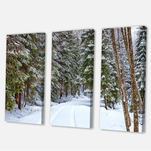Designart Snowy Road in the Forest Canvas Wall Art featuring a triptych of three gallery-wrapped cotton canvas panels depicting a snow-covered winding road through a dense forest of snow-dusted evergreen trees, printed with fade-resistant inks and arriving ready to hang, ideal for adding country charm to home décor.