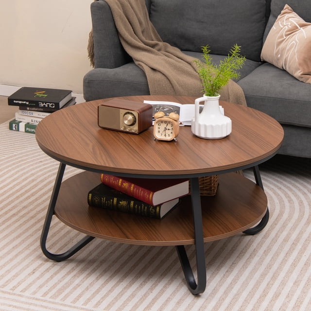 Giantex Table Basse Ronde, Table cocktail vintage à 2 Niveaux avec Fini grain de Bois Noyer et Tablette de Rangement Ouverte. Conçue avec un Cadre Métallique Robuste et des Patins de Pieds Ajustables pour la Stabilité. Exposée dans un Décor de Salon Douillet avec des Livres, une Horloge et un vase sur le Dessus de Table.