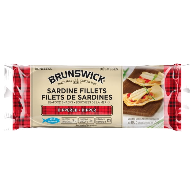 Brunswick Sardine Fillets - Kippered in a beige and red plaid package, featuring boneless smoked sardine fillets as seafood snacks with 18g protein, omega-3, and vitamin D per serving, plus a serving suggestion of fillets on crackers, suitable for quick nutritious canned fish meals.