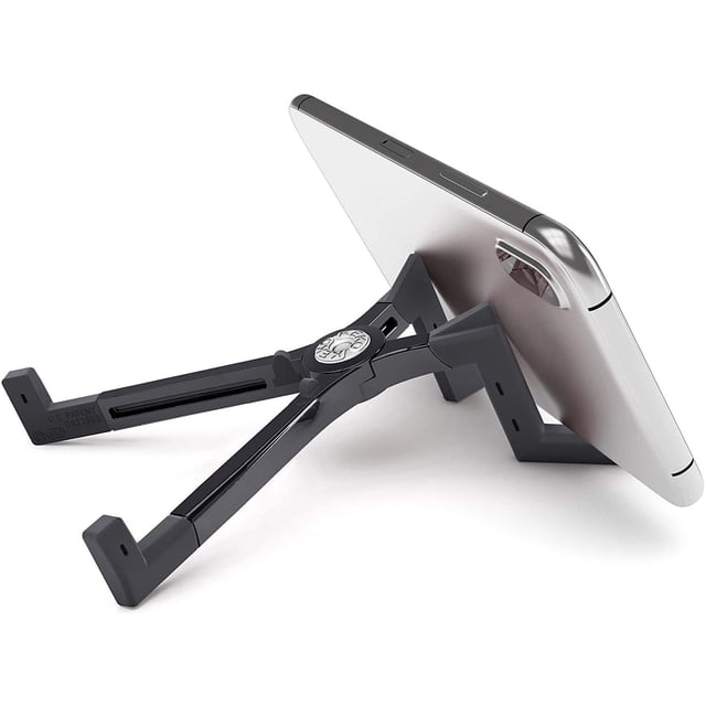 KEKO Universal Foldable Tablet Stand in black polycarbonate holding a silver tablet in landscape orientation from a 3/4 rear angle. The X-shaped stand features adjustable arms with anti-slip rubber pads, supporting tablets 4 to 13 inches with cases for ergonomic use on flat surfaces.