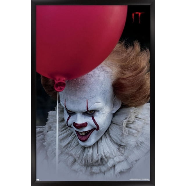 IT - Balloon Wall Poster, 14.725" x 22.375", depicting a close-up of cracked white face makeup with wild orange hair partially obscured by a large red balloon, set against a dark background with the red 'IT' logo in the top right corner, printed on glossy satin-finish poster paper and framed in black, ideal for horror-themed room decor or party decoration.