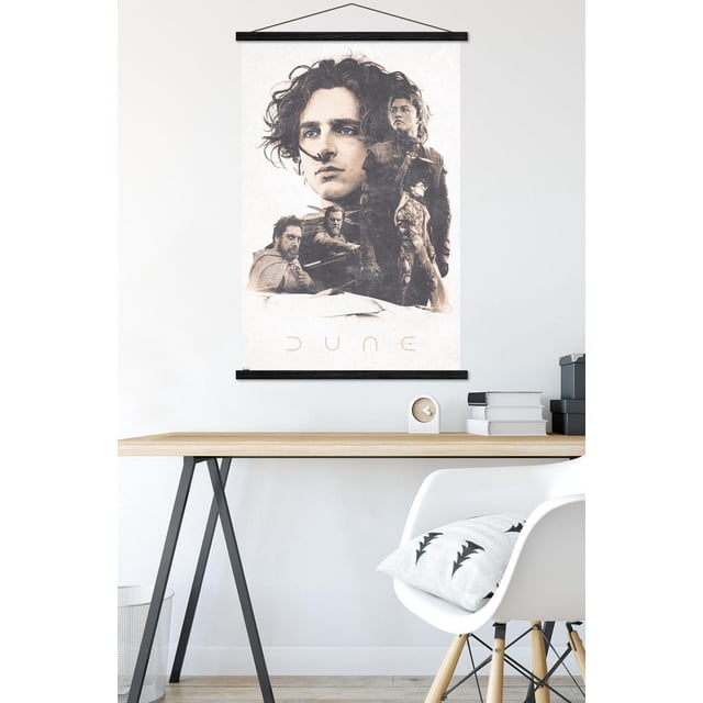 Dune: Part 2 - Group Wall Poster, 22.375" x 34", hanging on a white wall above a minimalist wooden desk with black metal legs. The glossy poster features high-resolution artwork of multiple characters from the Dune: Part 2 movie arranged in a layered composition with the title 'DUNE' at the bottom. The desk holds a small clock, stacked books, and a black storage box, with a white chair and patterned cushion nearby.
