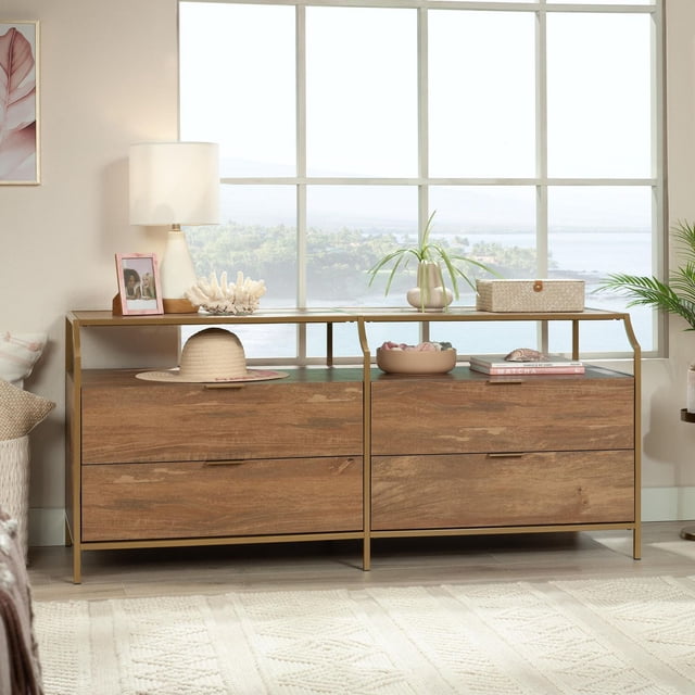 Sauder International Lux Commode à 4 Tiroirs, Fini Mangue Sindoori, avec Cadre en Métal satin Doré et Dessus en Verre Trempé de Sécurité, Dotée de Quatre Tiroirs Spacieux et d'Une Tablette Ouverte, Décorée d'Une Lampe, d'Une Plante, d'Un Chapeau et d'Articles Décoratifs dans une Pièce Lumineuse avec Grande Fenêtre Surplombant la Verdure et l'Eau.