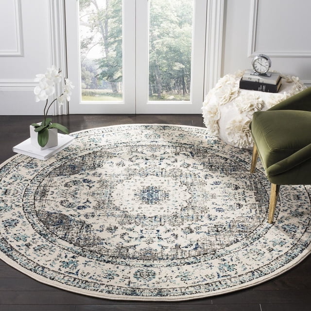 SAFAVIEH Evoke Tapis Traditionnel Teale, un Tapis Rond en Polypropylène Tissé Mécaniquement avec un Motif floral Crème, Bleu et Gris Usé, Posé sur un Plancher de Bois Franc Foncé Près de Portes Françaises Blanches, style avec une Chaise en Velours Verte et un pouf Texturé Blanc avec des Livres et une Horloge, Idéal pour Ajouter un style Décontracté et une Durabilité aux Espaces de Vie.