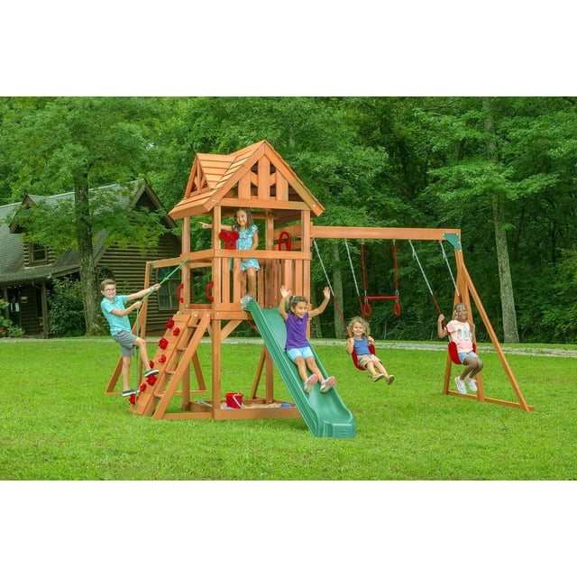 Ensemble de Jeu en Bois Style Chalet avec Toit en Bois - Multi Comprenant une Tour en Cèdre Massif avec une Terrasse de 4 Pieds, une Glissade Verte, un Mur d'Escalade, une Échelle en Bois et des Balançoires Rouges Côte à Côte. les Enfants Jouent Activement sur la Glissade, les Balançoires et le Mur d'Escalade dans une Cour Arrière Gazonée avec des Arbres et une Cabane Rustique en Rondins à Proximité.