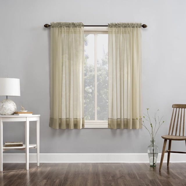 SUN TEXTILE VOILE POLE TOP CURTAIN in beige sheer crushed voile fabric with built-in rod pockets, hanging on a dark curtain rod over a window, softly filtering light while enhancing privacy in a modern room with gray walls, wood flooring, a white side table with a lamp and books, and a wooden chair next to a glass vase with branches, suitable for layering on a double rod for light control.