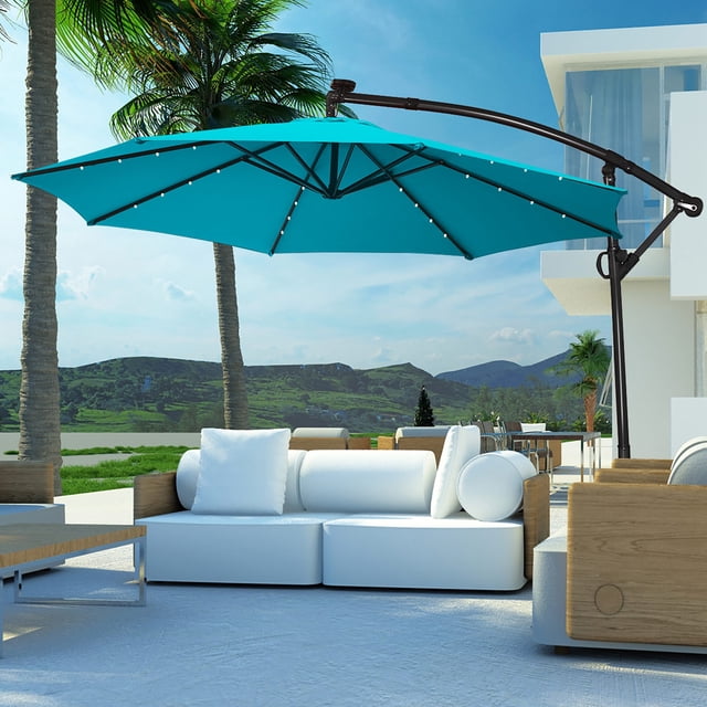 Costway 10FT Patio Offset Umbrella Solar Powered LED 360Degree Rotation Aluminum Turquoise. This outdoor umbrella features a 10-foot turquoise polyester canopy supported by 8 steel ribs and a powder-coated aluminum pole. It includes 24 solar-powered LED lights, with 3 lights on each rib, for nighttime illumination. The umbrella offers 360-degree rotation and an adjustable tilt mechanism for optimal shade. A vented canopy design promotes airflow, and a crank handle allows for easy opening and closing. Shown in a modern patio setting with white and wooden furniture, ideal for gardens, poolside, or outdoor lounging.