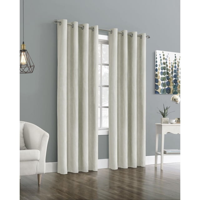 Emerald Blackout Grommet Indoor Curtain in light neutral color hanging on a silver metal rod with round grommets, covering a window in a modern living room with grey walls, wooden floor, a white armchair, a side table with a plant and cup, and abstract wall art. This energy-efficient blackout curtain features thermal insulation and noise reduction properties, suitable for creating a restful environment.