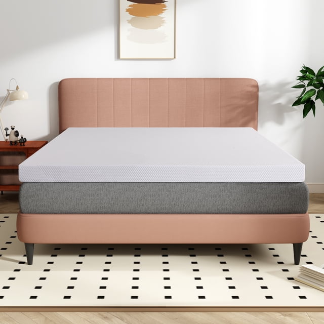 Telino 3 inch Full Mattress Topper, Memory Foam Mattress Topper with Removable & Washable Cover, White. The image shows a white memory foam mattress topper placed on a grey mattress, set on a modern bed frame with a pink upholstered headboard. The topper features a smooth, textured surface and is designed for comfort and support. The room includes a patterned rug, a wooden side table with decor, and a potted plant, creating a cozy bedroom setting.