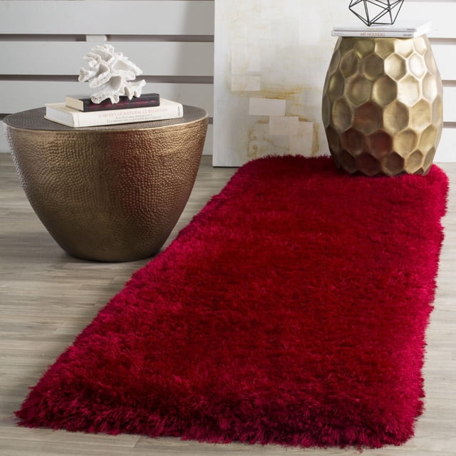 Safavieh Luxe Paxton Solid Plush Shag Area Rug, Red, 2'3" x 8' runner on a light wood floor between two metallic side tables with hammered bronze and honeycomb gold finishes. The deep red plush shag rug is made from soft synthetic yarns for comfort and durability, ideal for contemporary or country-chic decor and suitable for adding warmth to hallways or entryways.