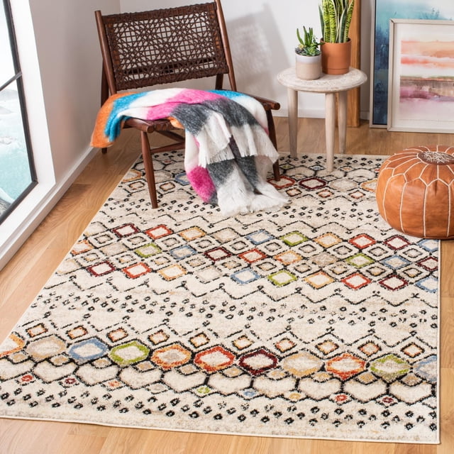 SAFAVIEH Amsterdam Gladwin Geometric Area Rug with a cream background and vivid multicolored tribal diamond patterns in red, blue, green, orange, and yellow, placed on light hardwood flooring. Styled with a woven wooden chair draped with a colorful throw, a round wooden side table with potted plants, and a brown leather pouf, suitable as an accent rug for rustic-chic décor.
