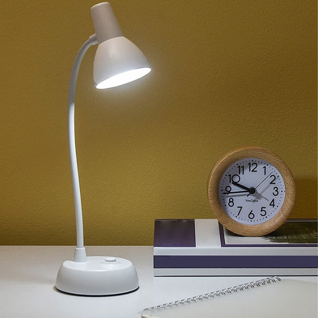 EQWLJWE desk lamp for bedroom featuring a compact white plastic design with a flexible 360° adjustable hose light pole. The lamp emits soft, natural light suitable for bedside reading or studying. It is battery-powered, requiring three AA batteries (not included), and includes a data cable. The lamp is shown on a white desk with a yellow wall background, accompanied by a wooden clock and books.