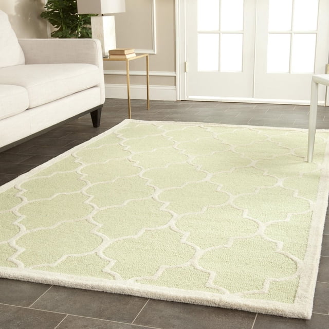Safavieh Cambridge Kevin Geometric Area Rug in light green wool with a cream raised geometric trellis pattern, hand-tufted with plush cut and loop piles, placed on a dark tile floor in a bright living room with a beige sofa and gold side table near white French doors, ideal for adding texture and modern American style to home decor.