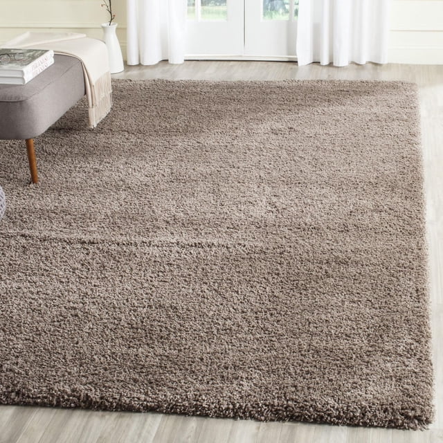 Safavieh California Solid Plush Shag Area Rug in taupe with a dense 4.5kg/m² polypropylene pile, placed on light wood flooring in a bright room with white curtains and a gray bench, embodying a casual West Coast style accent rug suitable for living rooms and often used as a soft floor layer for seating or play.