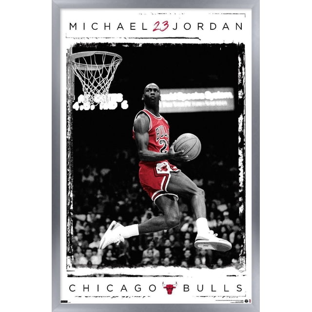 Michael Jordan - Dunk Wall Poster, 14.725" x 22.375" Framed showing Michael Jordan in a red Chicago Bulls jersey number 23 mid-air dunking a Spalding basketball near the hoop, with a black and white crowd background, framed in silver with Chicago Bulls text and logo below, suitable for sports-themed home décor.