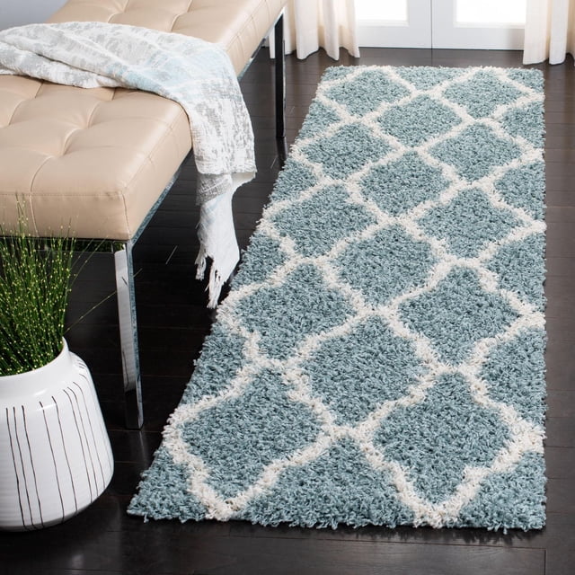 Safavieh Tapis Shag Géométrique Dallas Logan Bleu avec Motif de Carreaux Marocains Ivoire, Polypropylène Tissé Mécaniquement avec Poils Doux et Moelleux, sur Plancher de Bois Franc Foncé à Côté d'Un Banc Capitonné beige et d'Un Cache-Pot Blanc, Idéal pour Ajouter Confort et style aux Entrées Ou aux Couloirs.