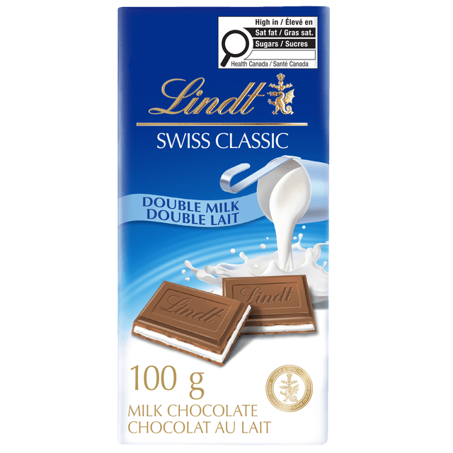 Lindt SWISS CLASSIC Double Milk Chocolate Bar, 100 grams, with a blue and white wrapper featuring the gold Lindt logo. The packaging shows two milk chocolate squares with a smooth creamy white filling and a splash of milk pouring from a silver jug, highlighting the double milk chocolate. The label includes bilingual text and a Health Canada nutritional warning. This Swiss chocolate bar is suitable for gifting or personal indulgence.