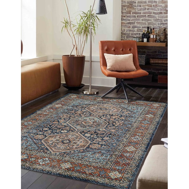 ECARPET Alicia Traditional Area Rug with warm and navy tones in a vintage geometric pattern, placed on dark hardwood flooring in a living room with a brown leather swivel chair, beige cushion, tall potted plant, floor lamp, and exposed brick wall with shelves.