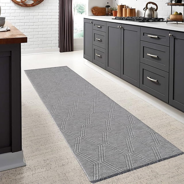 BY COCOON 2'x10' runner rug in a modern kitchen setting. The washable rug features a grey geometric pattern with a low pile thickness of 0.2 inches, making it ideal for high-traffic areas like entryways and hallways. Made in Turkey with durable, stain-resistant cotton and chenille materials, it includes a non-slip backing for added safety. Suitable for homes with kids and pets, this rug protects delicate flooring and is easy to clean with vacuuming or machine washing.