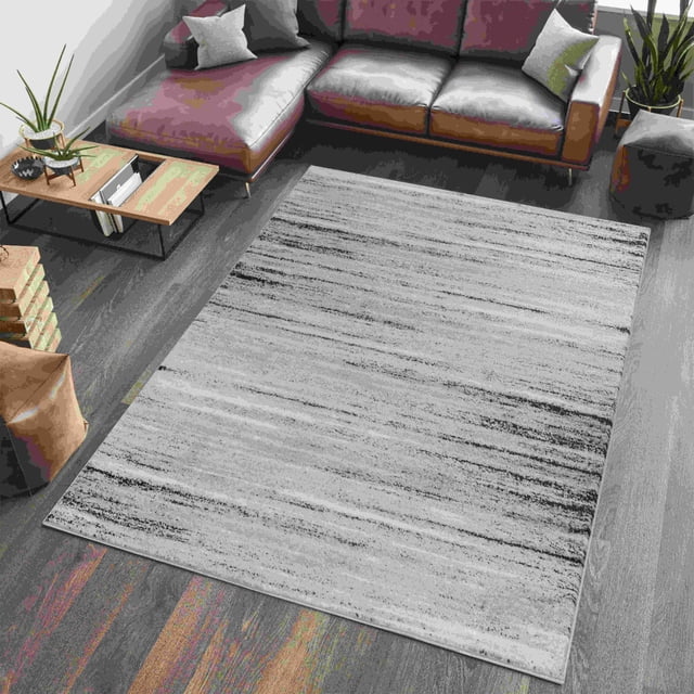 Rug Branch Sakarya Collection Tapis d'Intérieur Abstrait pour Aire, avec une Faible Hauteur de Poil de 0,3 Po et un Motif Abstrait Gris et Noir, Posé sur un Plancher de Bois Franc Foncé dans un Salon avec un sofa Sectionnel en Cuir Brun, une table Basse en Bois et des Plantes Vertes. Convient aux Zones Très Passantes et Polyvalent pour Chambres Ou Bureaux.