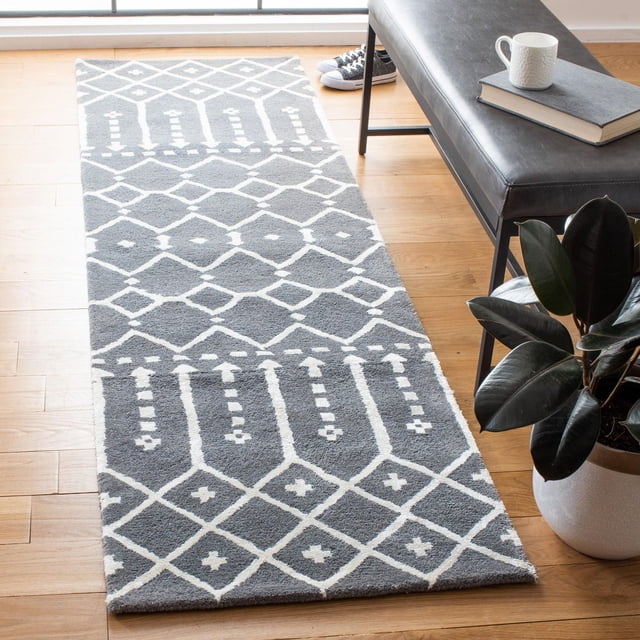 Safavieh Himalaya Darin Geometric Area Rug in light grey with white geometric diamond and linear patterns, crafted from 100% hand-loomed wool, placed on a hardwood floor next to a black leather bench with a book and white mug, near a potted plant, ideal for modern runner rug use.