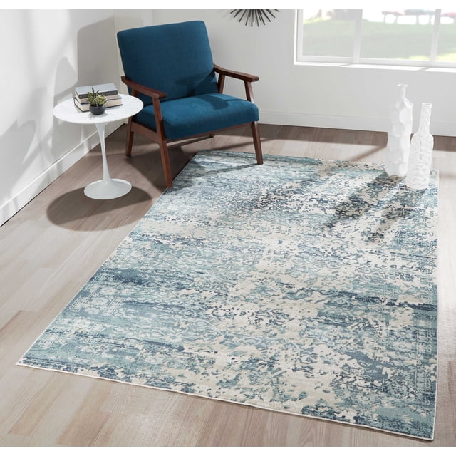 ECARPET Delphine Traditional Area Rug with distressed floral and ornamental patterns in blue and gray on beige, placed on light hardwood flooring in a bright room with a blue mid-century modern armchair, white round side table with books and a small plant, and two white decorative vases near a window, ideal for living rooms and high-traffic spaces.