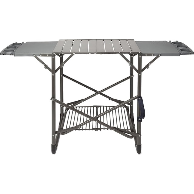 Cuisinart Take Along Portable Grill Stand 54" x 20" with a matte dark grey aluminum frame, fold-flat design, two flip-up side tables featuring six cup holders and eight tool hooks, a lower storage shelf supporting up to 35 lbs, and a ballistic nylon carrying handle for easy transport and setup without tools, suitable for outdoor BBQ cooking and entertaining.