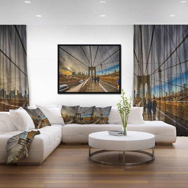 Designart Promenade sur le Pont de Brooklyn Cadre Flottant ART Mural Mettant en Vedette une Impression sur Toile Encadrée de Piétons Marchant sur l'Allée en Bois du Pont de Brooklyn avec la skyline de la Ville au Coucher du Soleil, Exposée dans un Salon Moderne avec Rideaux Imprimés Assortis, Oreillers et Couverture Jetée, Mettant en Valeur le style Industriel et les Tons Bruns.