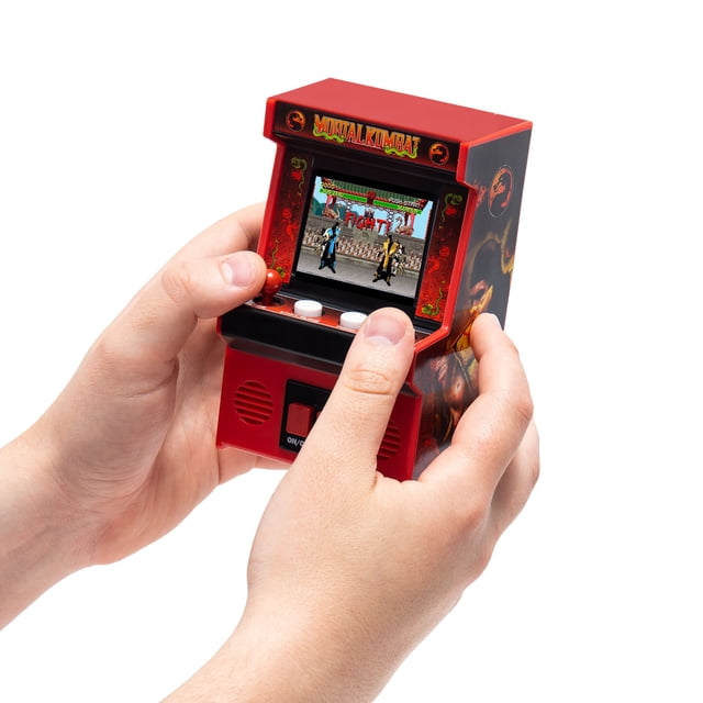 Basic Fun Mortal Kombat Mini Classique Console Portative Arcade Rouge, Tenue à Deux Mains, avec un joystick et Deux Boutons Blancs sous un Écran Pleine Couleur Montrant une Scène de Combat de Mortal Kombat Pixélisée avec des Personnages Classiques et des logos sur les Côtés, Convient aux Jeux Rétro en Déplacement.