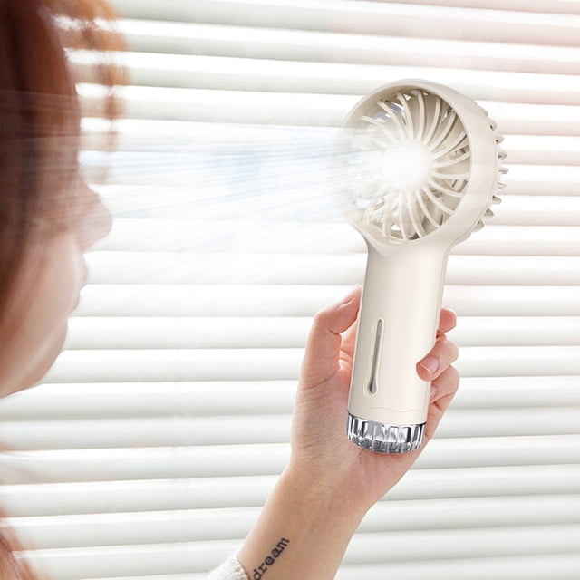 TNDBKQWR Fans Portable Rechargeable Hand Held Fans for Women Mini Personal Fan shown in use. The compact handheld fan features a beige body with a transparent base and emits a visible stream of air. Designed for portability, it includes USB rechargeable functionality, a misting feature for enhanced cooling, and is suitable for use as a table or desk fan in travel, office, and outdoor settings.