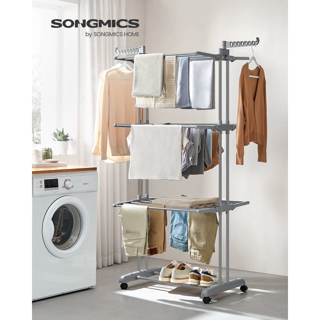 SONGMICS Clothes Drying Rack Stand 4-Tier in gray, made of durable steel and plastic with reinforced double rods for stability. The rack features three top tiers, two rotating wings with 14 slots, and a bottom tier for shoes. It is displayed in a laundry room with clothes, towels, and shoes arranged on it. The rack has four casters, two with brakes for secure placement, and is foldable for easy storage. Dimensions are 25.2 inches deep, 49.6 inches wide, and 67.7 inches high when unfolded.