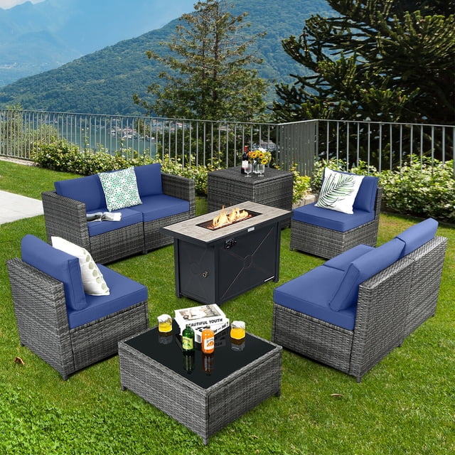 Gymax 9 PCS Patio Rattan Furniture Set Fire Pit Table Storage Black W/ Cover Navy centered front view of a navy PE rattan sectional with four armless and two corner seats, removable navy cushions, 42" propane fire pit table with lava rock and tempered glass surface, powder-coated steel frames, matching storage box and protective covers; suitable for backyard entertaining and often used to store cushions or provide extra seating.