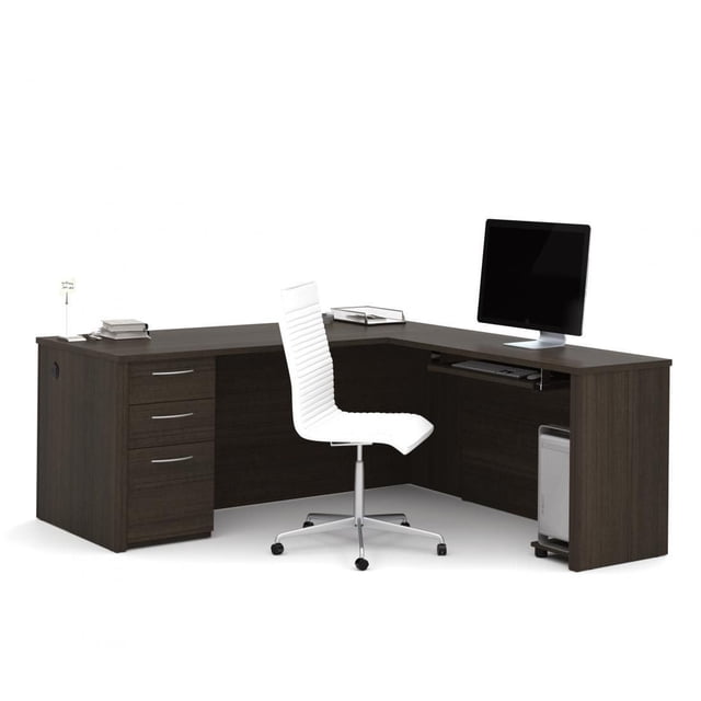 Bestar Embassy 71" L-shaped desk in dark wood finish with a 1-inch commercial grade melamine surface, three drawers with silver handles, a full modesty panel, and a keyboard tray. A white ergonomic swivel chair is positioned in front, with a computer monitor and tower on the desk. The desk features wire management grommets and meets ANSI/BIFMA standards, ideal for home office use and organizing office equipment.