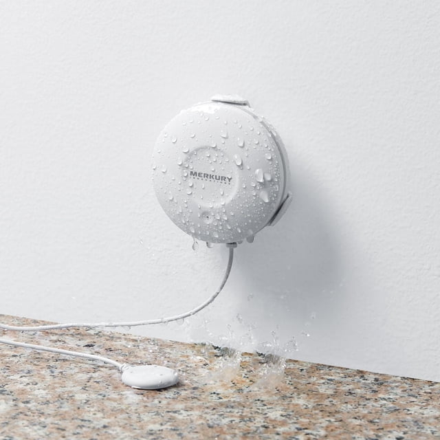 Merkury Innovations Capteur d'Inondation Intelligent Wi‐Fi avec Boîtier Rond Blanc Monté sur un Mur Blanc, Recouvert de Gouttes d'Eau, Connecté par un Câble Blanc à un Petit Capteur Ovale sur un Comptoir en Granit, Conçu pour Détecter les Fuites d'Eau et Envoyer des Alertes via Wi‐Fi.