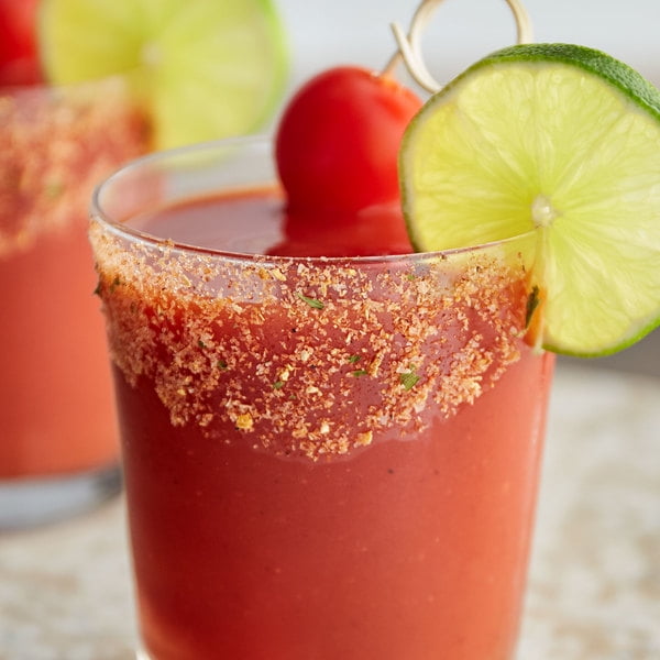 Rokz 5 oz. Bloody Mary Margarita/Cocktail Rimming Salt used to garnish the rim of a glass filled with a vibrant red Bloody Mary cocktail. The rim is coated with a blend of over 12 all-natural spices, adding a zesty and flavorful touch. The drink is garnished with a lime wedge and a skewer of cherry tomatoes, creating a festive presentation.