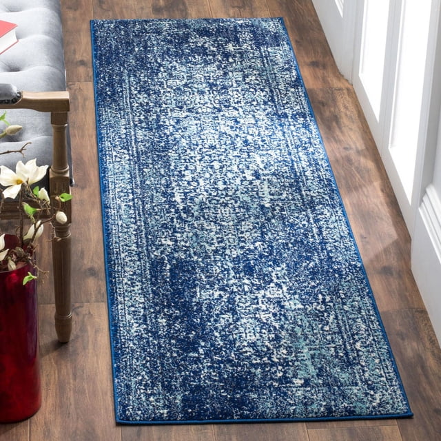 Safavieh Evoke Trena Traditional Area Rug with a blue and white distressed painterly pattern, made of power-loomed polypropylene frieze yarns, placed on hardwood flooring beside a gray upholstered chair and red vase, suitable as an accent rug for hallways or entryways.
