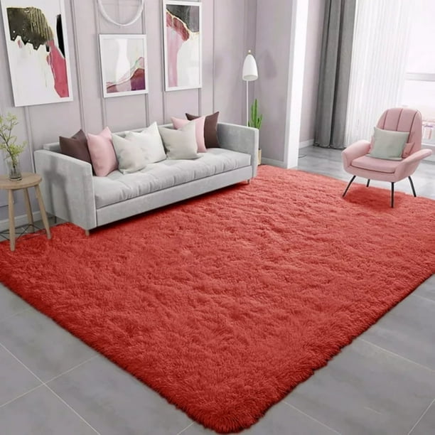 HueMaison 5 x 7 ft Shaggy Area Rugs for Bedroom Living Room Large Fluffy Floor Carpet Rugs Home Décor in red. The rug features a super-soft velvet surface, a 2-inch thick supportive sponge interlayer, and a PVC non-slip bottom for stability. It is displayed in a modern living room with a grey sofa, pastel cushions, and a pink accent chair, creating a cozy and elegant atmosphere. Suitable for wooden or tile floors, it is easy to clean and ideal for living rooms, bedrooms, or kids' rooms.