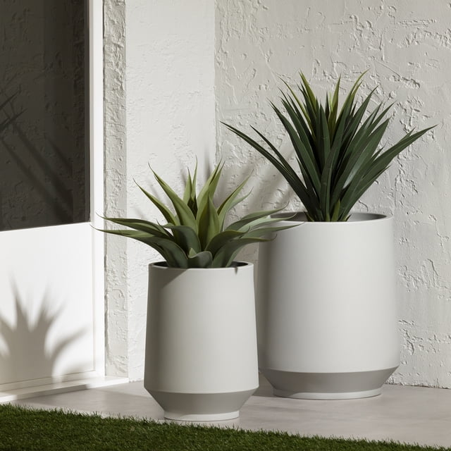 South Shore Dalya Set of 2 Planters in greige, two cylindrical polyethylene pots with matte finish, one 12 1/4 in and one 16 1/4 in diameter, placed on a patio floor against a textured white wall with green artificial plants, suitable for indoor and outdoor garden use.