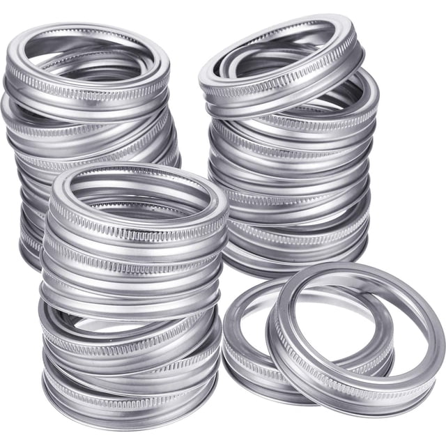 24 pieces of regular mouth canning jar replacement metal rings in silver, made of durable tinplate material. These practical screw jar bands are leak-proof and compatible with mason jars. The rings measure approximately 70 mm in outer diameter and 56 mm in inner diameter, suitable for sealing jars to keep food fresh. The image shows multiple stacks of the metal bands with a smooth, grooved design for airtight sealing.