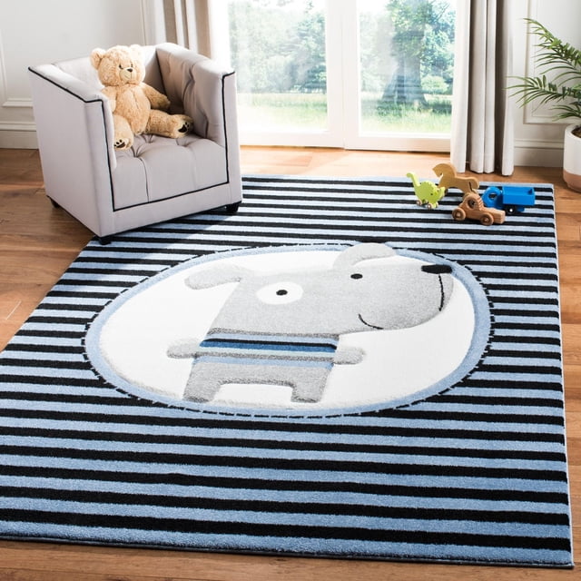 Safavieh Carousel Kids Orpa The Dog Area Rug showing a cartoon grey dog with blue stripes inside a white oval on a black and blue striped background. This durable synthetic yarn kids rug lies on a hardwood floor near a grey armchair with a teddy bear and wooden toys, suitable for kids' room decor and play areas.