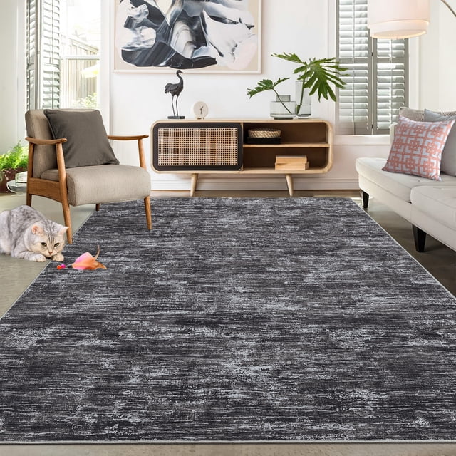 Garvee 6'x9' Modern Abstract Area Rugs Washable Rug in dark gray displayed in a contemporary living room setting. The rug features a low-pile, stain-resistant surface with a modern abstract design, complemented by a non-slip TPR backing for safety. It is placed under furniture, showcasing its thin profile and suitability for high-traffic areas. The room includes neutral-toned furniture, a decorative console, and natural light streaming through shutters.