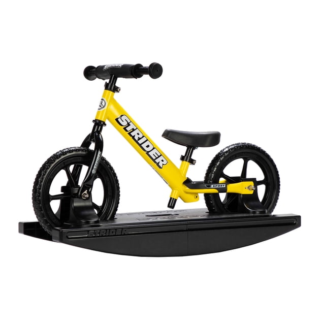 Strider 12 Sport 2-in-1 Rocking Bike in yellow, designed for children aged 6 months to 5 years. The bike is securely mounted on a black rocking base, allowing babies to develop balance and coordination. The lightweight frame features toddler-sized grips, a cushioned seat, and adjustable handlebars. The bike can be detached from the base for use as a balance bike, with never-flat tires and a seat height range of 30-48 cm (11-19 in.).