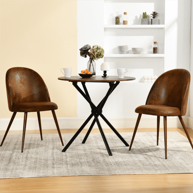 Homy Casa set of 2 armless dining chairs with curved brown faux suede upholstered backs and thickly padded seats, paired with a round wooden table with black metal tripod legs, set on a light grey patterned rug in a minimalist dining room with white shelves holding bowls and plants, ideal for small dining spaces.