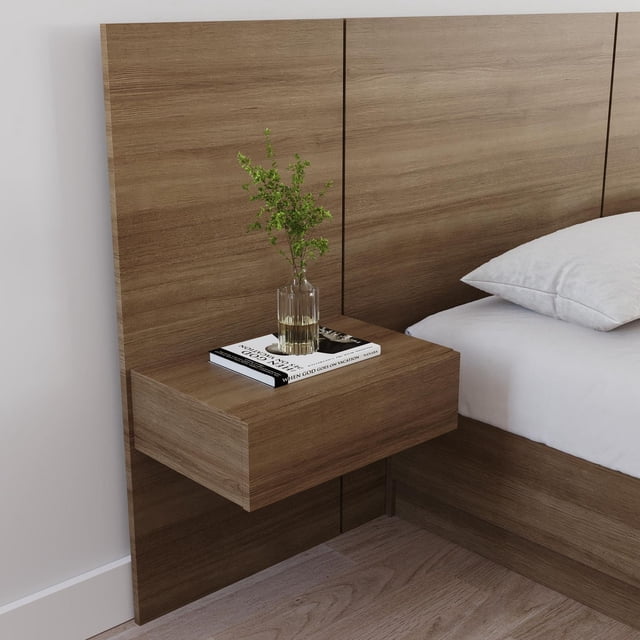 Nexera Milano Floating Nightstand Extension Panel in natural oak finish with integrated drawer, mounted on a matching headboard panel beside a bed with white bedding, featuring a clear glass vase with green foliage and a book on top, set against a light wall and wood floor, suitable for bedside storage and display.