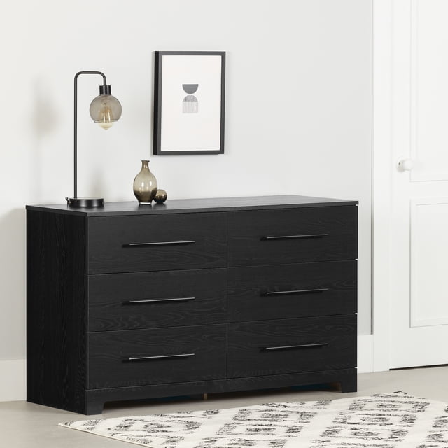 South Shore Primo 6-Drawer Dresser for Adult in black oak finish with six large drawers and metal handles, designed for bedroom storage, shown in a minimalist room with a light grey wall, framed abstract art, a black metal lamp, and decorative vases on top, standing on a light floor with a patterned rug.
