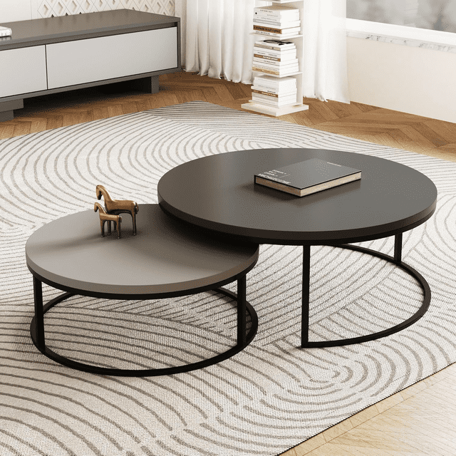 NessCarsti Ensemble Moderne de tables Basses Rondes Comprenant Deux tables Gigognes avec des Pieds en Métal Noirs et des Plateaux en Bois Gris. la Plus Grande Table a un Diamètre de 31,5 Pouces, la Plus Petite Mesure 23,7 Pouces et s'Empile en Dessous pour un Rangement compact. l'Ensemble Est Exposé dans un Salon Moderne avec un Tapis à Motifs et un Plancher en Bois, Mettant en Valeur Sa Conception Polyvalente et Peu Encombrante.