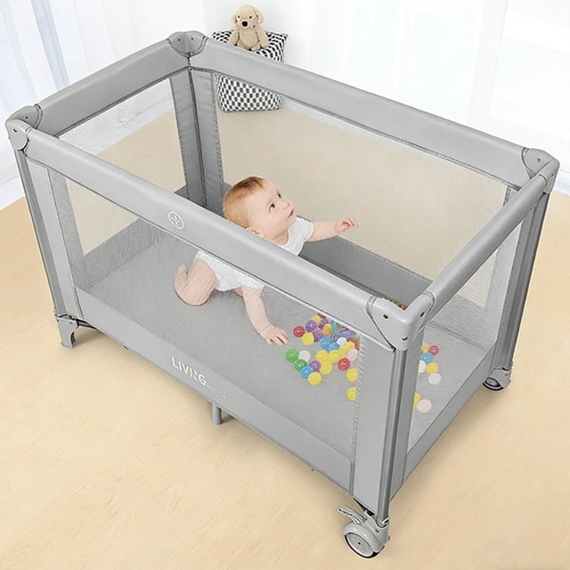 Foldable Baby Playard by LIVINGbasics in grey, shown in an unfolded state with a baby playing inside. The playard features a spacious design with dimensions of 49.21 x 25.59 x 30.71 inches, large mesh sides for 360° visibility, and two wheels for easy mobility. It includes a folding mattress pad and a carry bag for convenient storage and travel. Suitable for babies aged 0-36 months, with a weight capacity of 15kg (33lbs).