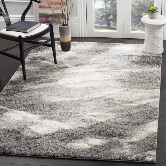Safavieh Retro Panit Abstract Area Rug with a mid-century modern abstract pattern in grey, cream, and beige tones, made of low pile polypropylene, displayed on dark hardwood flooring in a bright room with a black wooden chair, a gradient ceramic vase with branches, and a white ceramic garden stool holding a small succulent.