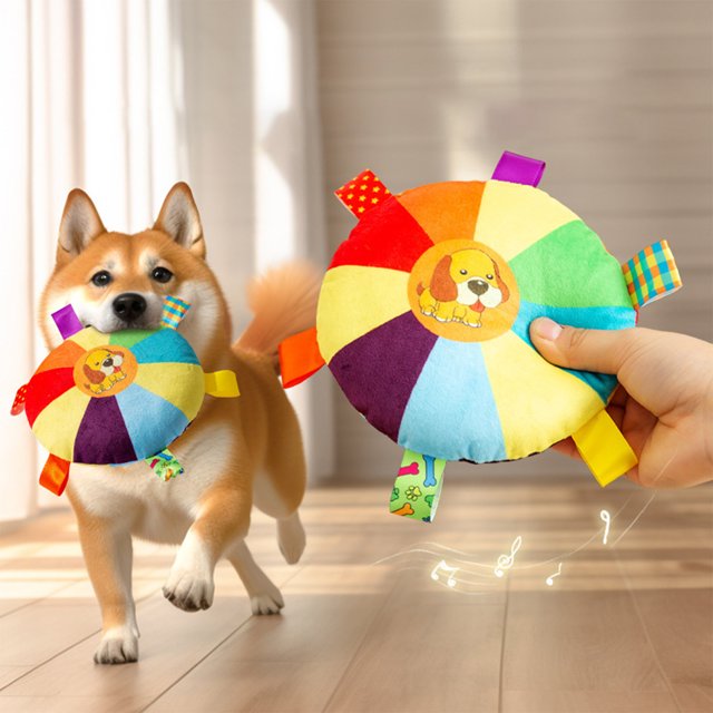 RKSTN Plush Objects Soft Dog Toy Bring and Catch Dog Toy Interactive Dog Chew Toy with Sound. A multicoloured plush flying disc toy with a dog illustration at the center, made of durable polyester and filled with polypropylene cotton. Designed for interactive fetch games and chew play, it features built-in sound to engage dogs. Suitable for dogs of all breeds and sizes, shown in a home setting with a dog actively playing.