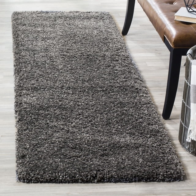 Safavieh California Solid Plush Shag Area Rug in dark grey with a dense 4.5kg/m² polypropylene pile, rectangular and plush, placed on a light wood floor beside a brown leather bench and woven basket, ideal for adding softness and warmth to home interiors or accent spaces.